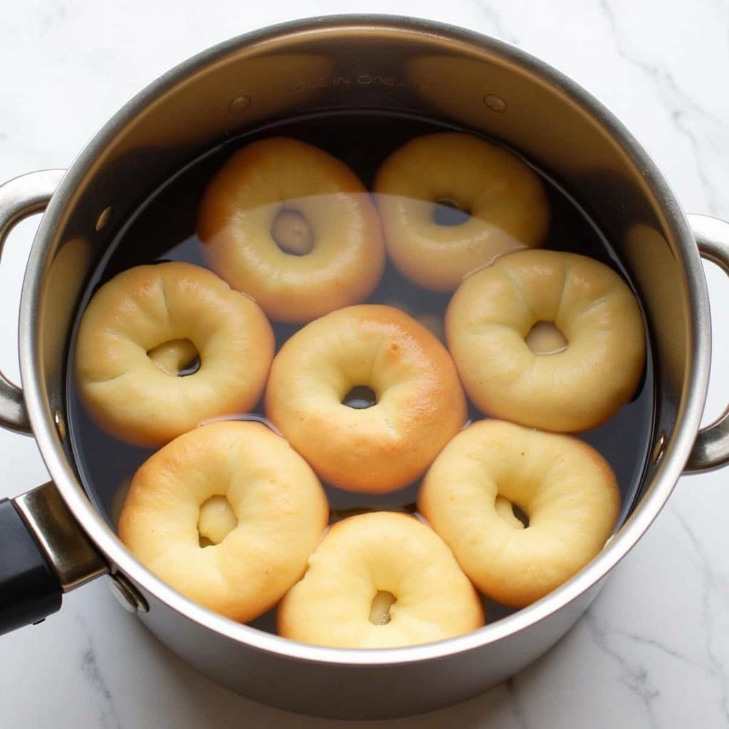 Gluten-free sourdough bagels being boiled in a pot of simmering water.